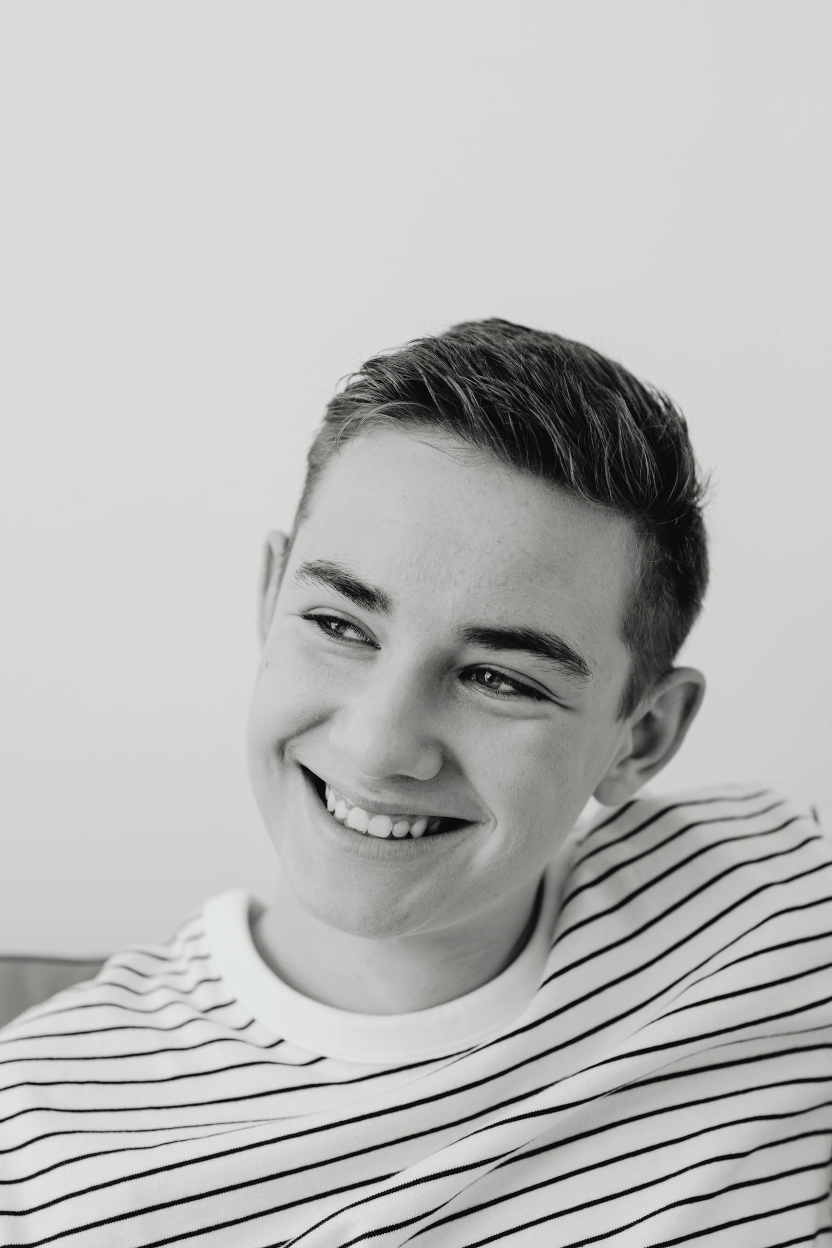 Close-up black and white portrait of a smiling young man in a striped shirt.